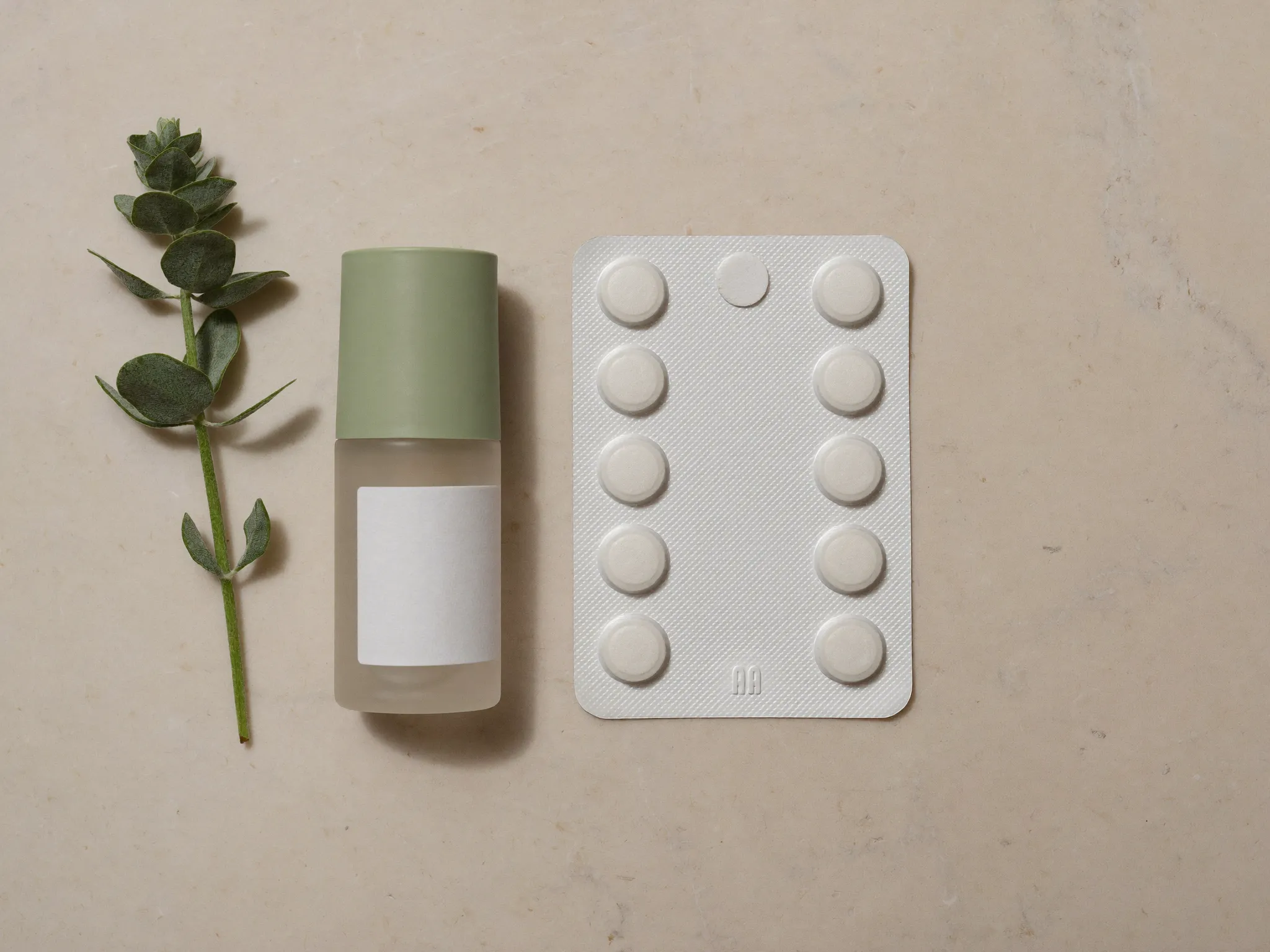 A frosted glass vial and a blister pack of tablets on a stone surface