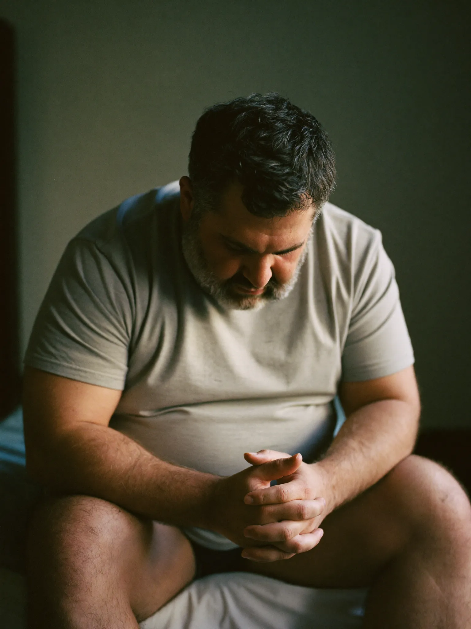 Marcus sitting on the edge of his bed at dawn, weighed down in thought