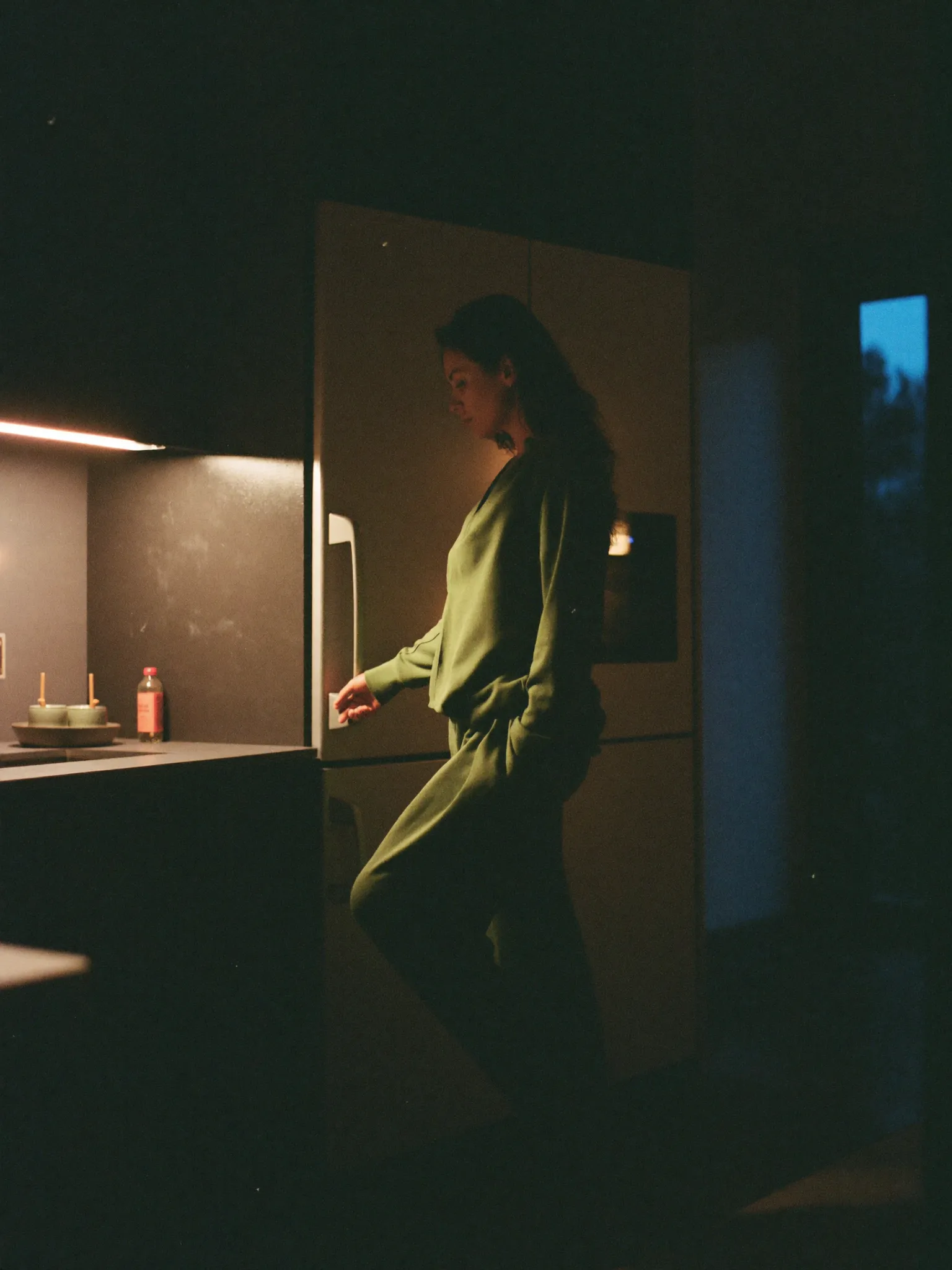 A woman standing in a dim kitchen at night, deep in thought